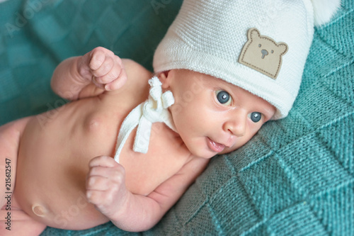 Cute naked newborn baby with white woolen hat. Funny caucasian baby with big widely opened blue eyes.