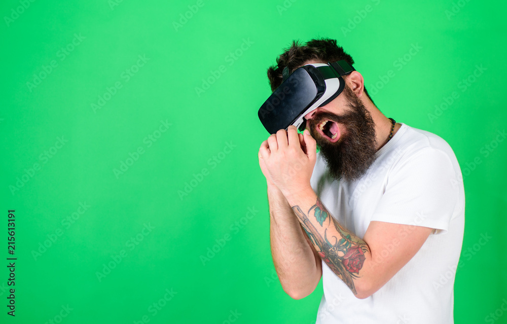 Man with beard in VR glasses, green background. Hipster on busy face use modern technologies for entertainment or education. VR musician concept. Guy with VR glasses singing with imaginary microphone Man with beard in VR glasses, green background. Hipster on busy face use modern technologies for entertainment or education. VR musician concept. Guy with VR glasses singing with imaginary microphone