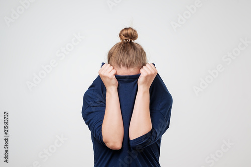 European woman hiding face under the clothes. She is oulling sweater on her head. photo