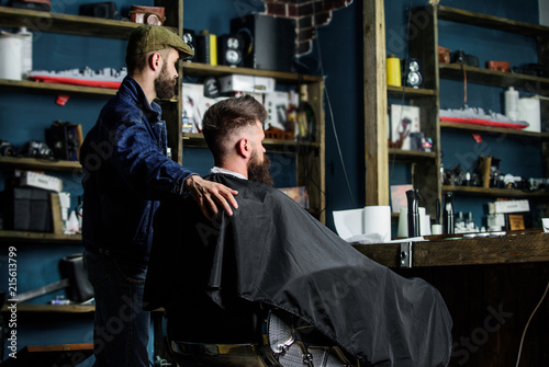 Hipster client got new haircut. Barber with bearded man looking at mirror, barbershop background. Haircut concept. Client and professional master checking result. Barber finished trimming