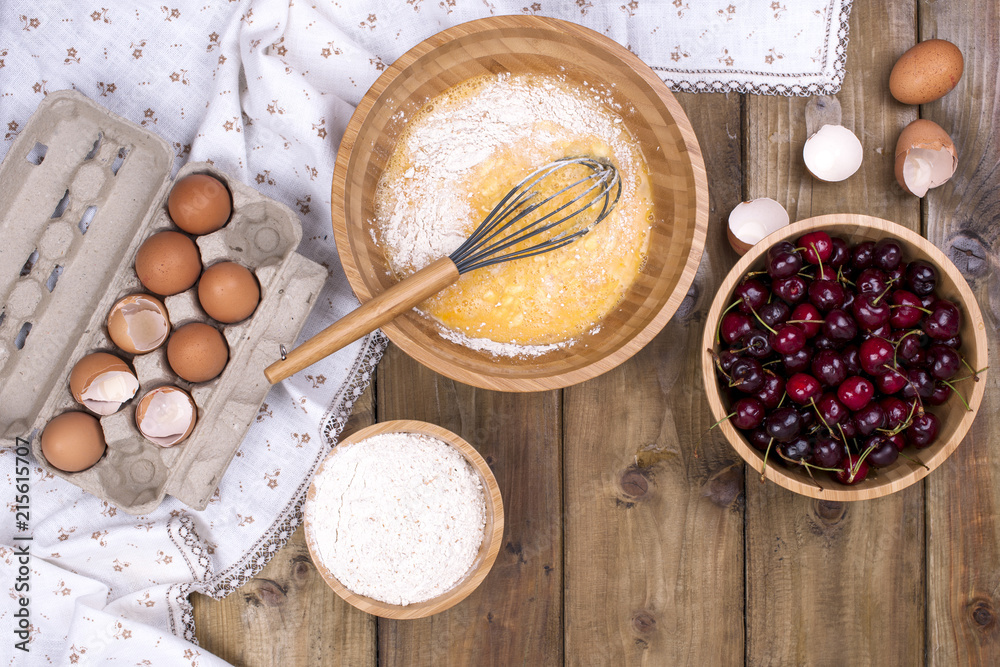 Preparation of homemade sweet pastries with cherries. Eggs, flour and berries on a wooden background. Flat lay, copy space,