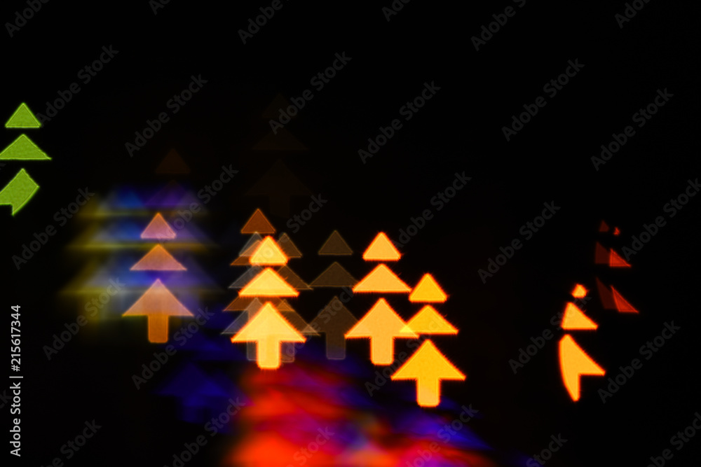 Obraz premium Lights of christmas garland blurred on black background. Lights of colorful garland blurred as beautiful background. Christmas holiday decoration with silhouette of christmas trees. Christmas concept