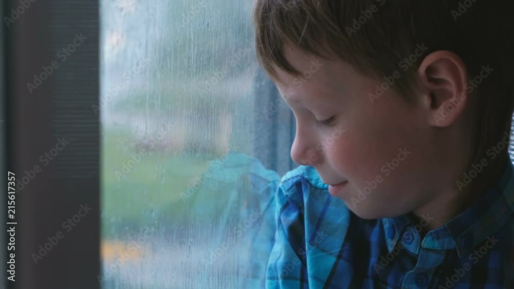 Boy looks out the window in the rain and is sad.