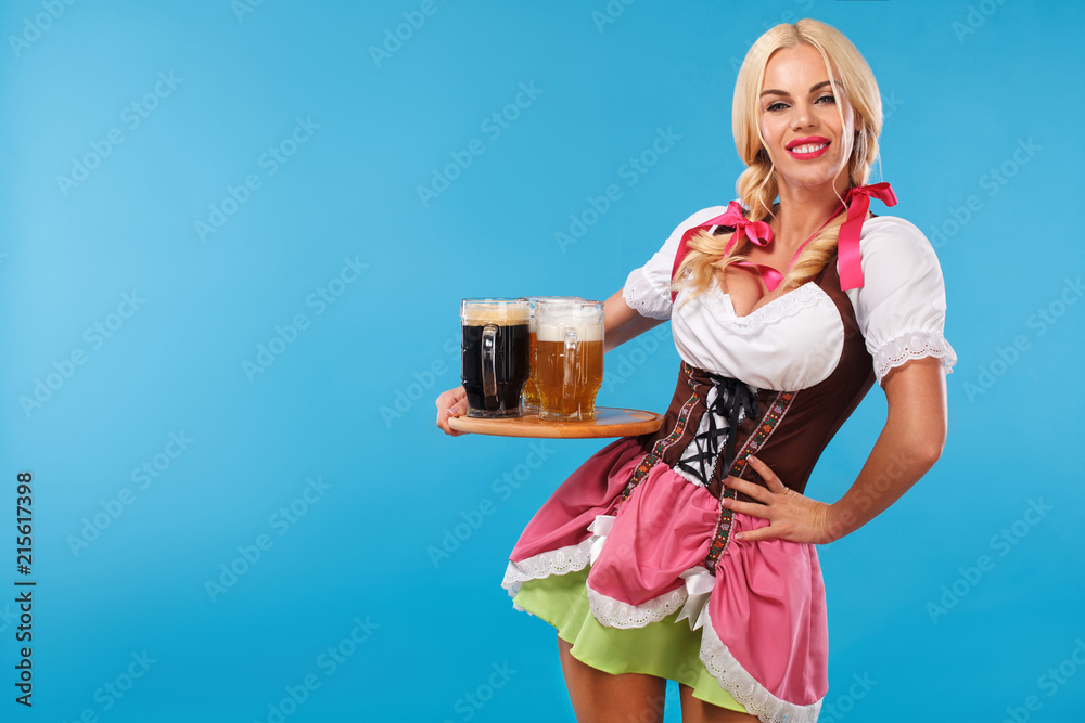 Young sexy Oktoberfest girl - waitress, wearing a traditional Bavarian dress, serving big beer mugs on blue background. Young sexy Oktoberfest girl - waitress, wearing a traditional Bavarian dress, serving big beer mugs on blue background.