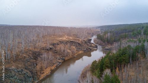 Aerial photoshot of Miass river in Ural, Russia in the late autumn evening with pine and birch trees on the banks of the river, it's snowing