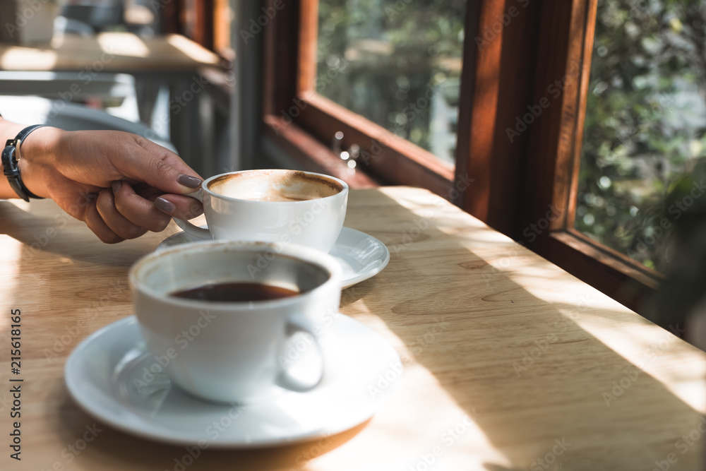 Closeup image of a hand holding a white cup of hot latte coffee on wooden table in cafe Closeup image of a hand holding a white cup of hot latte coffee on wooden table in cafe