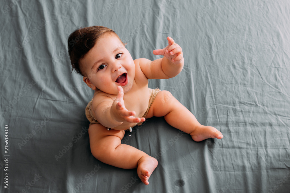 Top view of smiling baby sitting on the bed in the room wearing shorts - obrazy, fototapety, plakaty 