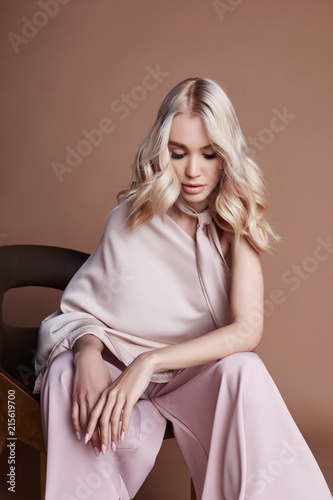 Sexy luxurious woman in a dress sitting on a chair. Autumn collection of women clothing. Fashion blonde in a long beautiful dress posing on background. Beautiful hair and a perfect girl figure