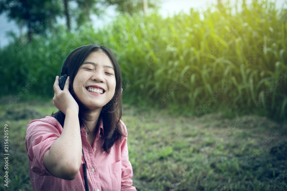 Asian girls beautiful concept headphones to relax. She was happily listening to music while sitting on the grass in the park. Asian girls beautiful concept headphones to relax. She was happily listening to music while sitting on the grass in the park.