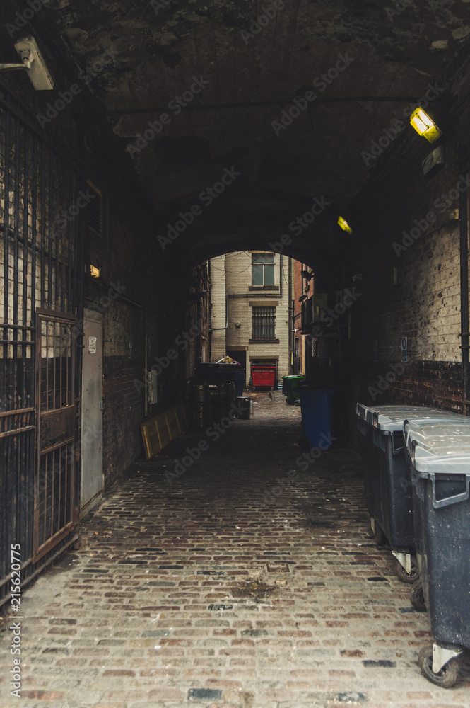Dark and old alley. Creepy passage with trash bins, windows and surveillance camera. Urban scene of Leeds, England, UK.