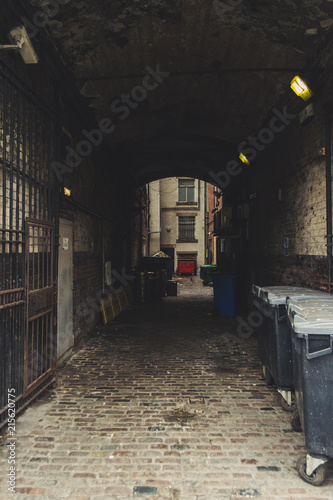 Dark and old alley. Creepy passage with trash bins  windows and surveillance camera. Urban scene of Leeds  England  UK.