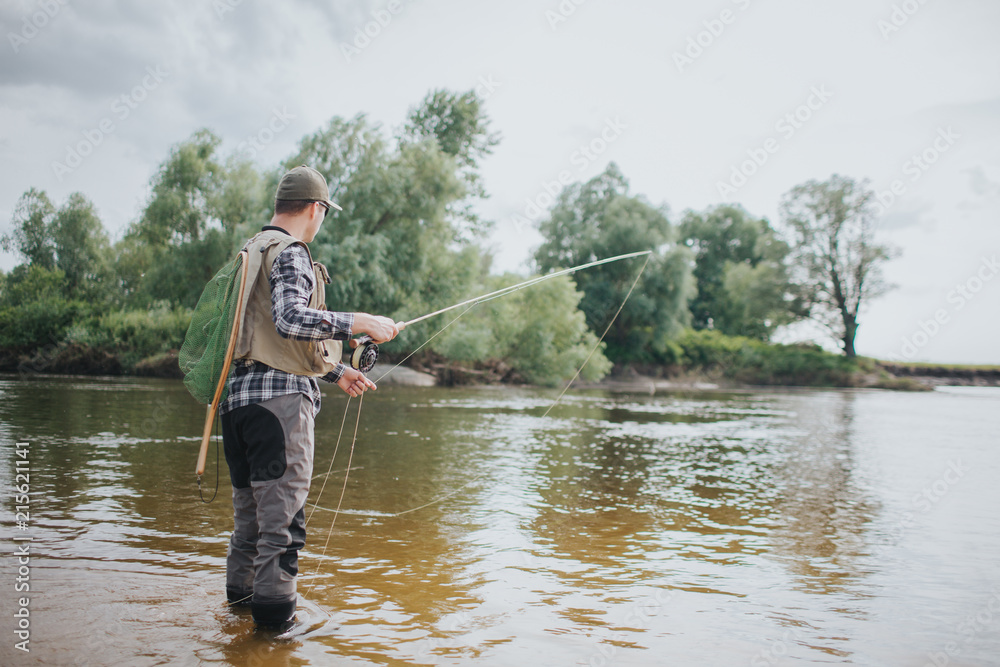 Adult stands in shallow and holding fly rod in hands. He is