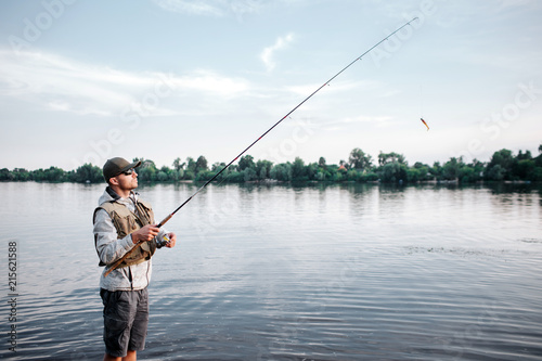 A picture of fishaerman standing in shallow and fishing. He holds fly rod. Guy looks up and forward. He is calm.