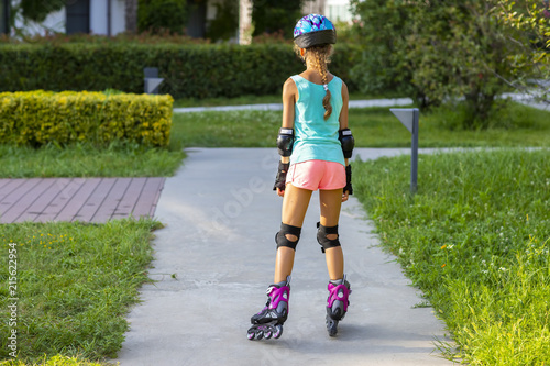 Back view of little girl in blue helmet and colorful sport clothes on roller-skates