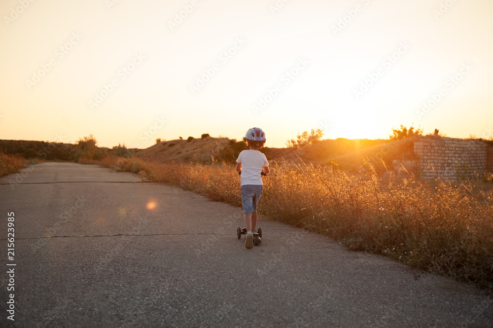 healthy little boy riding scooter on empty road on summer sunset