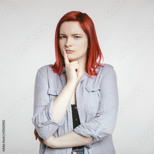 Red haired plus size ordinary woman standing on a neutral grey background. Emotional portrait. She looks thoughtful