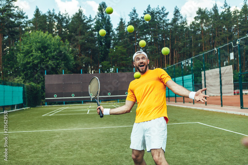Portrait of beaming man trying to hit a lot of ball while exercising in tennis game on court