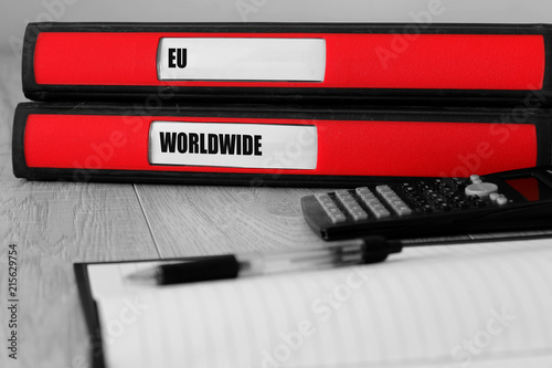 Red folders with eu and worldwide written on the label on a desk with selective colour