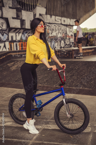Sexy slim fit brunette woman in sport casual outfit in a skate park. Active leisure on a bicycle