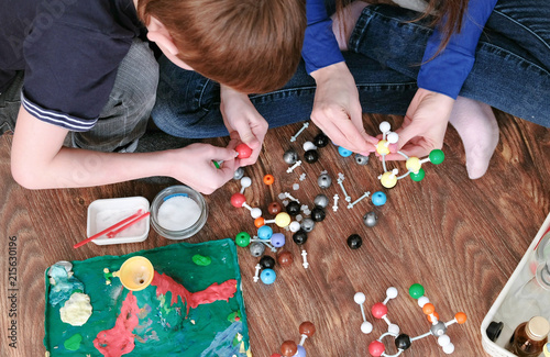 Closeup hands of mom and son building molecule models of colored plastic construction set. Top view.