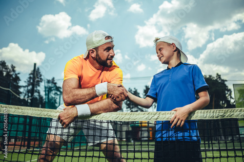Side view beaming man shaking hand of smiling kid during conversation after workout on field © Yakobchuk Olena