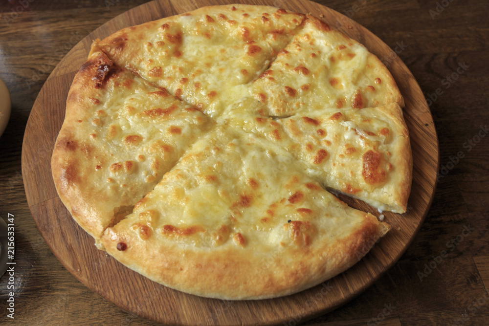 Fresh cheese pizza on a wooden plate on the table, Italian traditional appetizer, high angle view.
