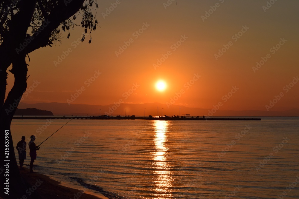 Silhouettes of fishermen fishing in Aegean Sea. Summer sunset in Greece