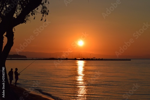Silhouettes of fishermen fishing in Aegean Sea. Summer sunset in Greece