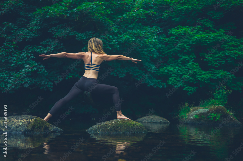 Yoga woman in warrior pose on rock in river Yoga woman in warrior pose on rock in river