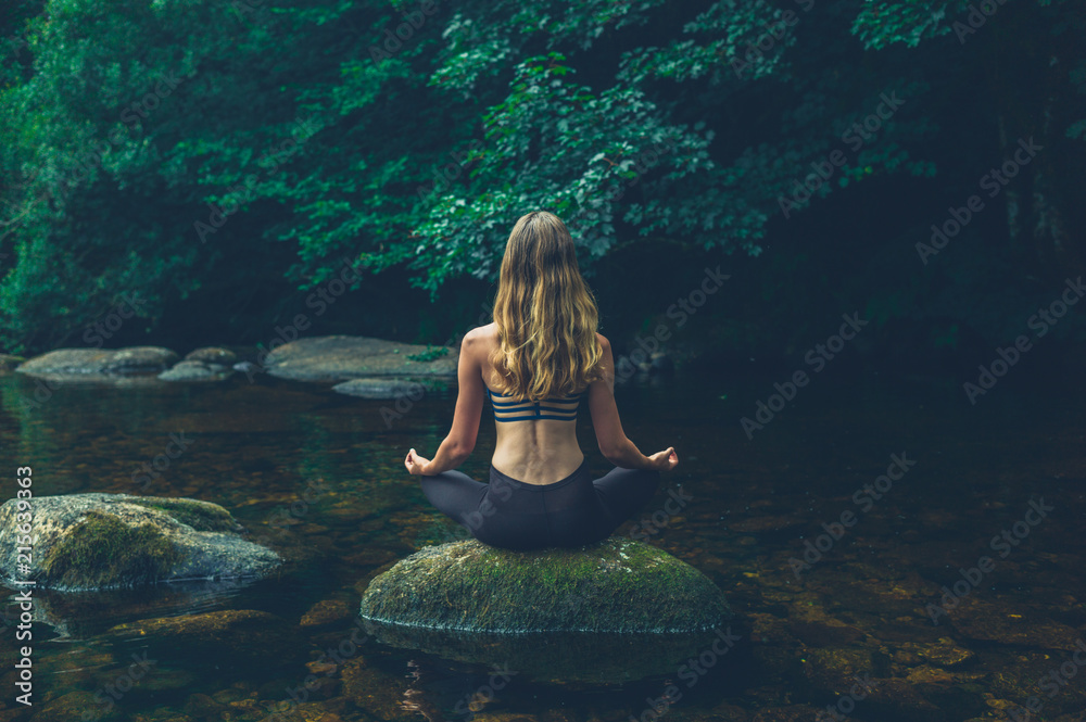 Woman meditating on rock in river - obrazy, fototapety, plakaty 