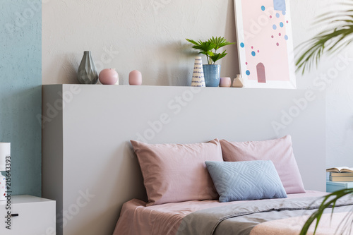 Poster on headboard of bed with pink pillows in bedroom interior with plants. Real photo photo