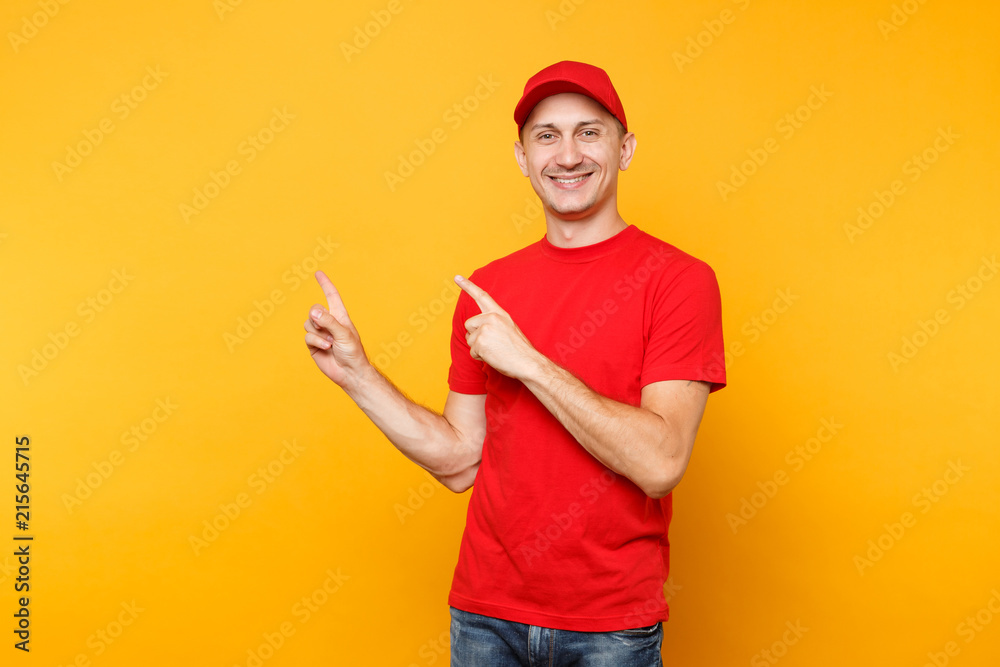 Delivery man in red uniform isolated on yellow orange background. Professional male employee in cap, t-shirt working as courier or dealer pointing index fingers aside on copy space. Service concept.
