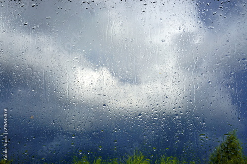 Raindrops on the glass and storm clouds in the background. Rainy weather forecast. © HENADZ