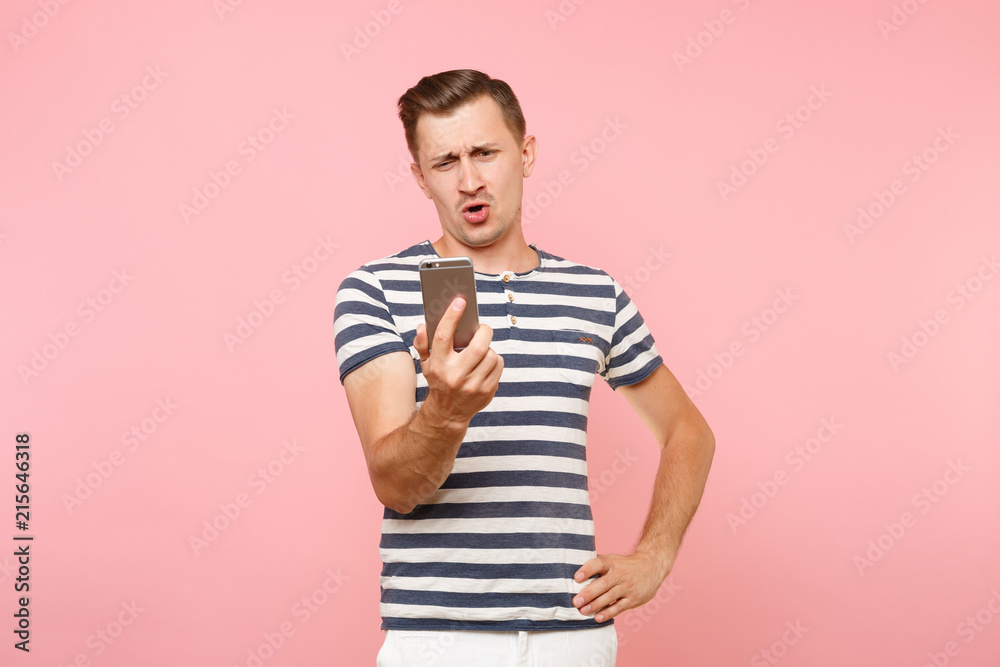 Portrait of sad angry shocked young man looking on display mobile phone, surprised sms You're fired, dismissal from work isolated on pastel pink background. People sincere emotions lifestyle concept. Portrait of sad angry shocked young man looking on display mobile phone, surprised sms You're fired, dismissal from work isolated on pastel pink background. People sincere emotions lifestyle concept.