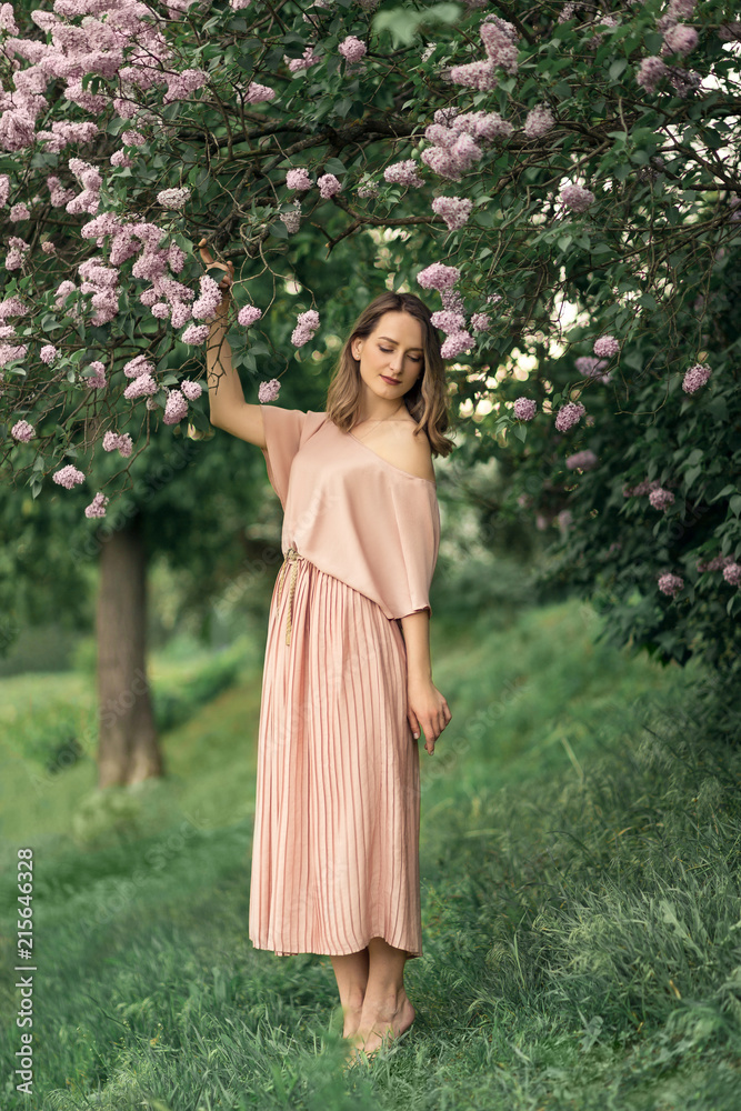 Young woman in a beautiful dress is standing near a lilac bush