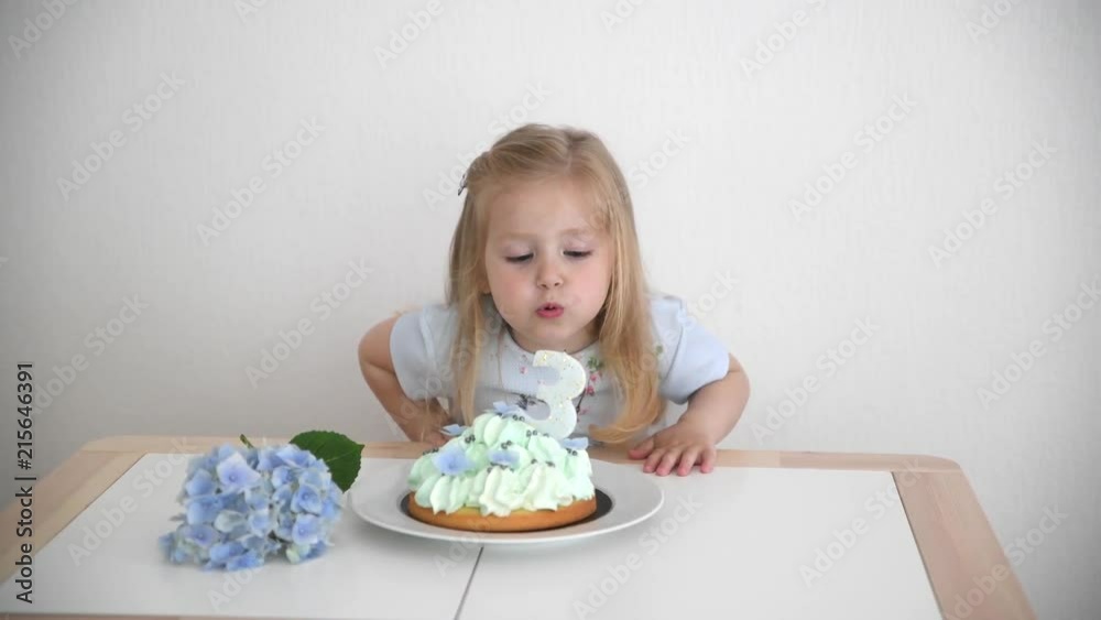 A girl of 3 years old making wish blowing candles on the blue cake A girl of 3 years old making wish blowing candles on the blue cake