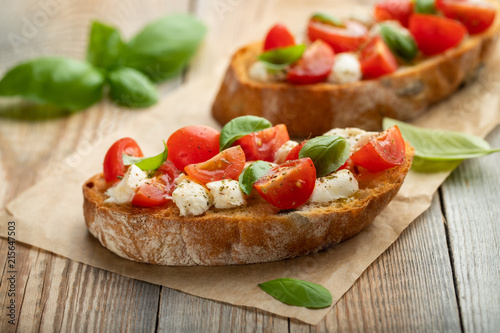 Bruschetta with tomatoes, mozzarella cheese and basil on a old rustic table. Traditional italian appetizer or snack, antipasto
