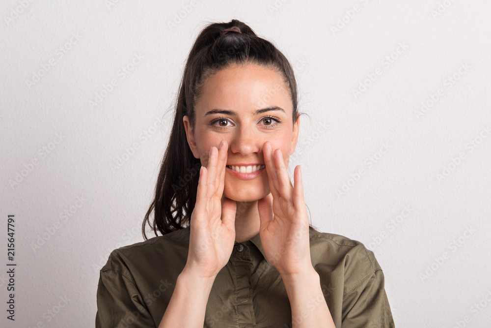 Portrait of a young beautiful woman in studio, hands cupped around her mouth. Portrait of a young beautiful woman in studio, hands cupped around her mouth.
