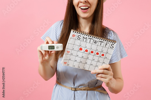 Smiling woman in dress hold in hand thermometer, female periods calendar for checking menstruation days isolated on pink background. Medical healthcare, ovulation gynecological concept. Copy space. photo