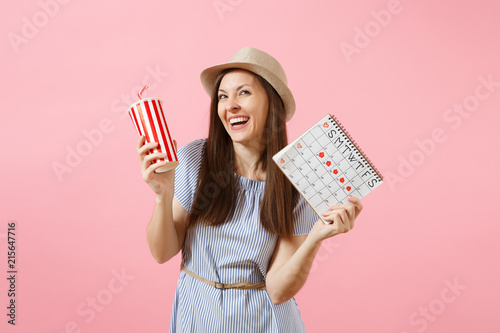 Portrait of happy woman in blue dress, hat holding cup of soda, female periods calendar for checking menstruation days isolated on pink background. Medical healthcare gynecological concept. Copy space