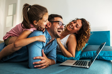 Happy family lying on bed and watching something on laptop. Laughing and having fun.	