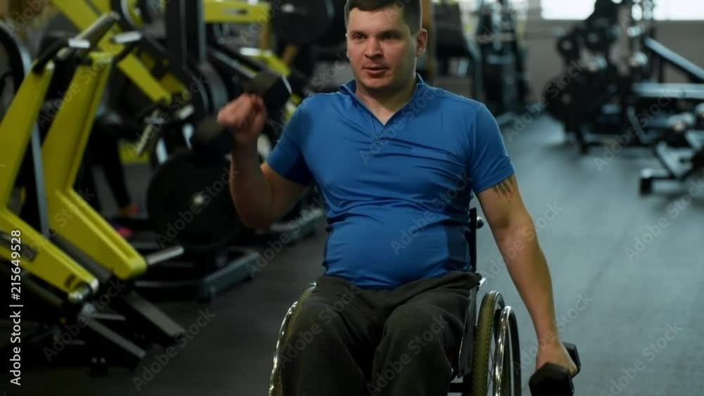 Tilt up of paraplegic man in wheelchair doing shoulder press with dumbbells in gym Tilt up of paraplegic man in wheelchair doing shoulder press with dumbbells in gym