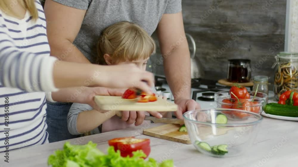 Tilt down of beautiful family cooking salad together at home: father cutting cucumber with cute daughter and mom slicing bell pepper Tilt down of beautiful family cooking salad together at home: father cutting cucumber with cute daughter and mom slicing bell pepper
