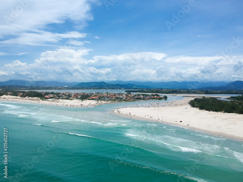  Aerial view of Brazilian beach with blue sky, white clouds, tourists in the sand, green and blue sea.
