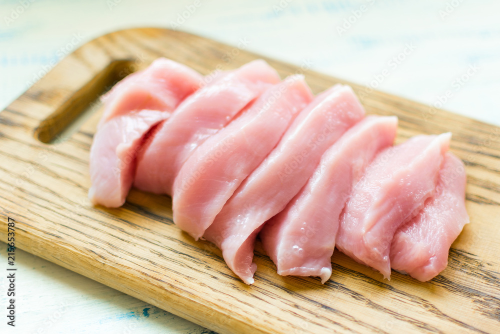 Raw meat fillet of turkey, chicken sliced on a wooden board.