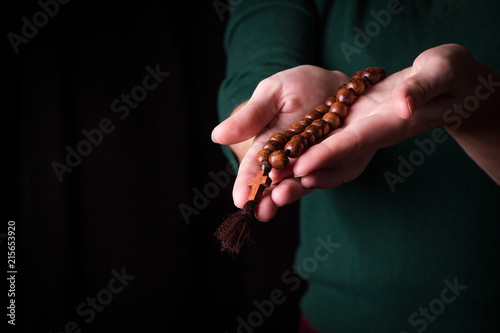 Rosary, cross   in female hands on a dark background. 