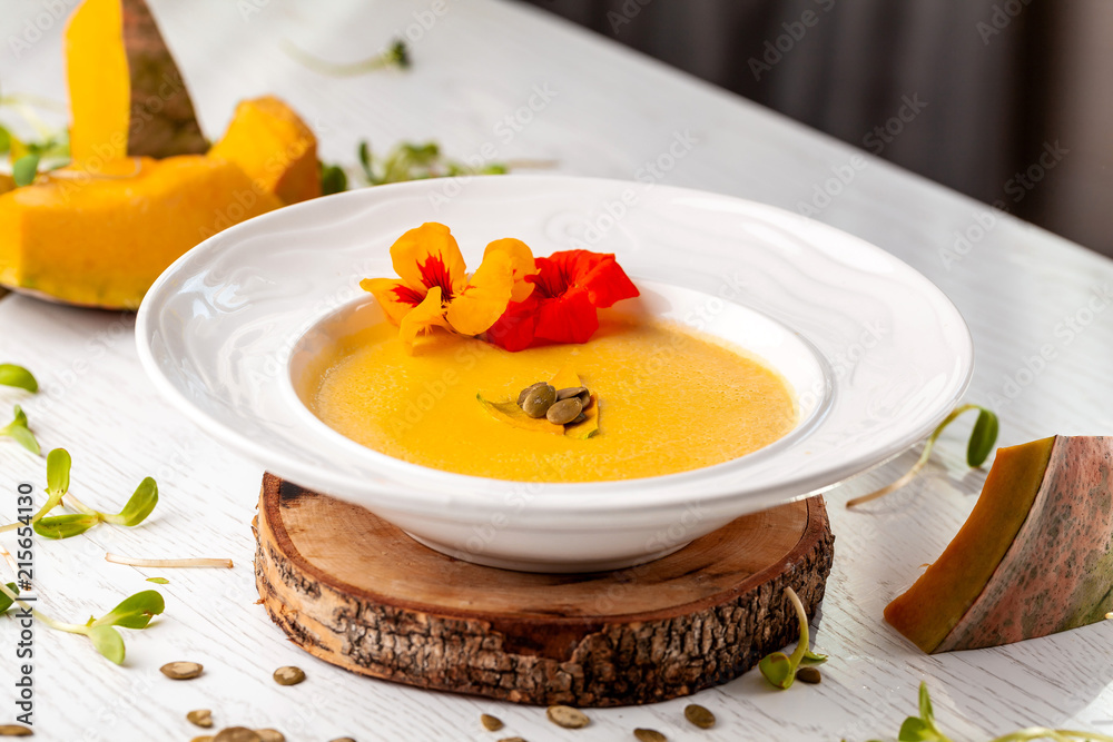 Ukrainian cuisine. Pumpkin puree soup, with cream, pumpkin seeds and flowers on a white plate. Copy space, selective focus Ukrainian cuisine. Pumpkin puree soup, with cream, pumpkin seeds and flowers on a white plate. Copy space, selective focus