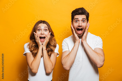 Image of young people man and woman in basic clothing screaming in surprise or delight and touching cheeks, isolated over yellow background photo