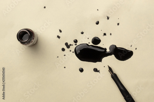 An overhead photo of an ink well with drops of ink and a nib pen, with copy space
