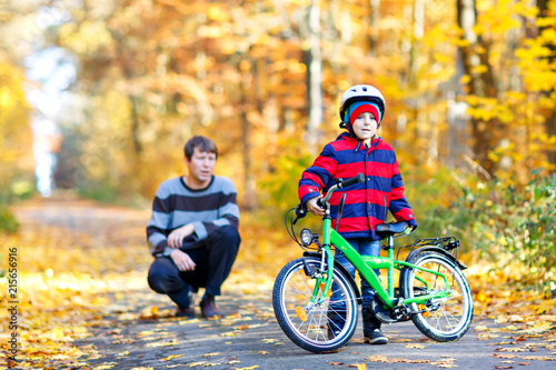 Little kid boy and his father in autumn park with a bicycle. Dad teaching his son biking